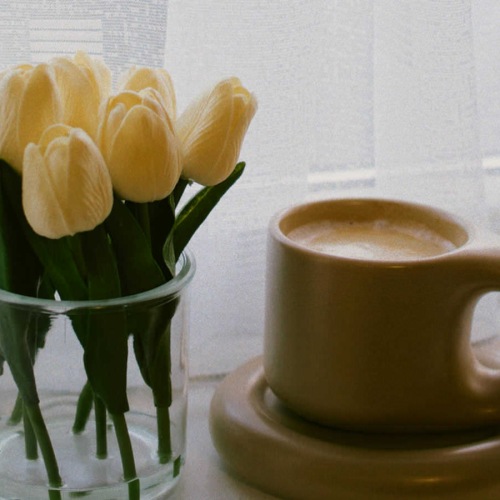 vase of tulips near a mug on a windowsill